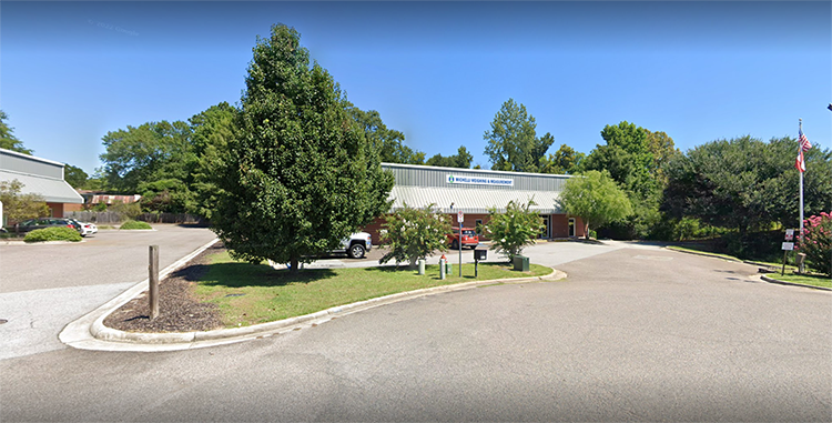 Aerial view of Michelli Weighing & Measurement Augusta Office. Red brick buildling with gray tin roof and a white sign that reads "Michelli Weighing & Measurement" surrounded by trees.