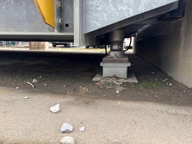 Photo showing underneath a truck scale. The load cell is visible, along with some debris that should be removed to allow the scale to move freely and ensure a longer truck scale life.